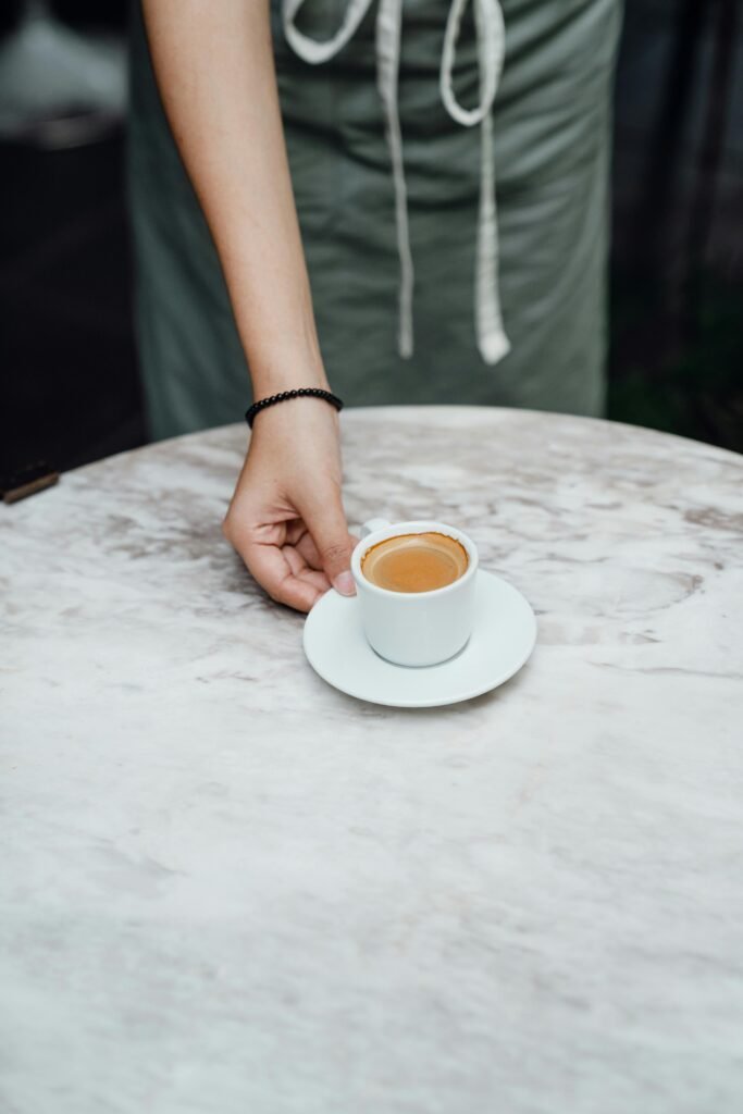 A barista serves a fresh espresso on a marble table in a modern café setting.