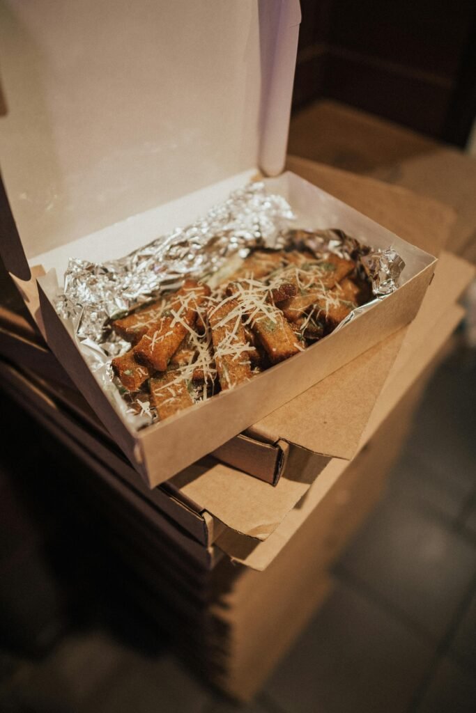 A close-up of fresh bread sticks topped with parmesan in a takeout box, perfect for snack time.